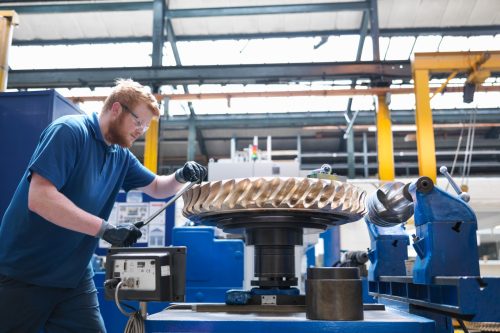 Engineer finishing bronze gear wheel in engineering factory